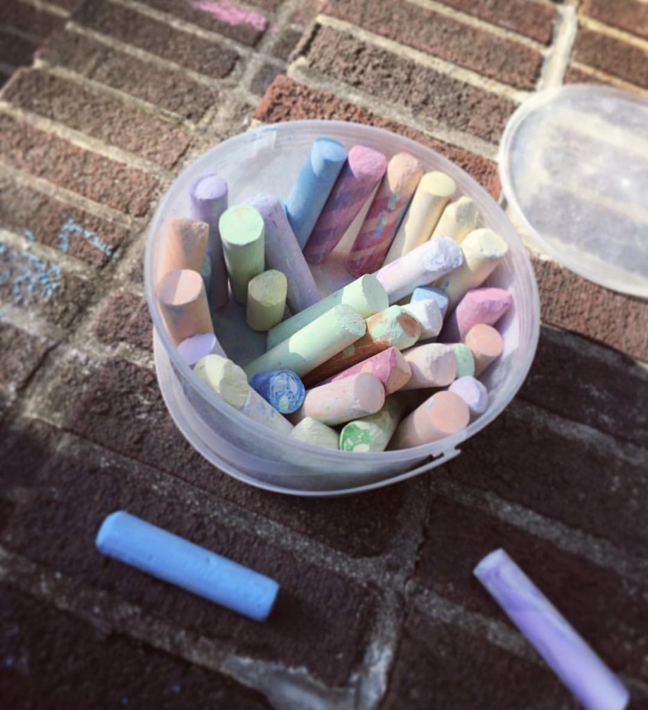 A bucket of pastel coloured chalk on a brick patio.